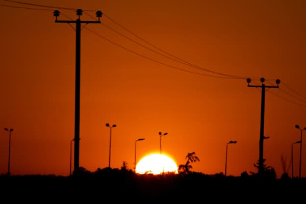 Photo of sun setting on horizon with silhouette of power lines in foreground