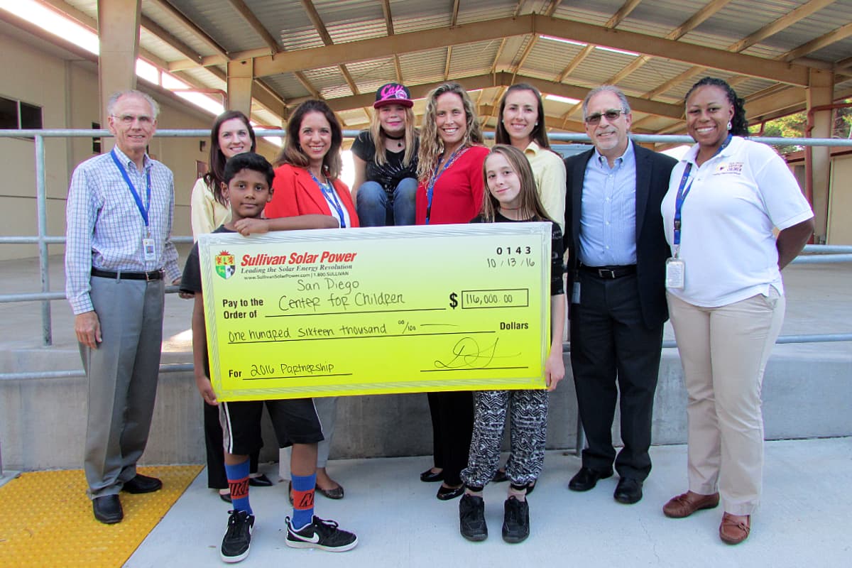 Photo of adults and children smiling holding oversized, celebratory donation check