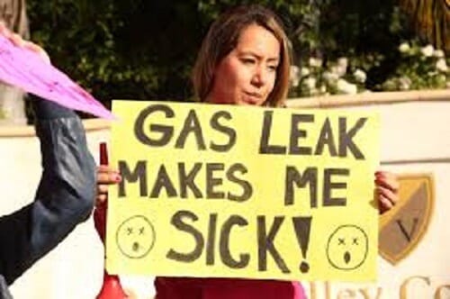 Photo of a female protestor holding sign stating Gas Leak Makes Me Sick