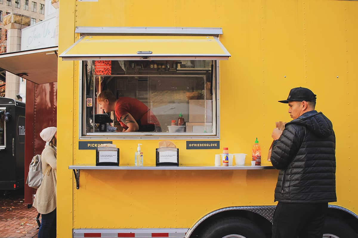Photo of vibrant yellow food truck with patrons ordering and enjoying a meal