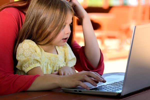 Photo of mother and her young daughter learning reading on a laptop