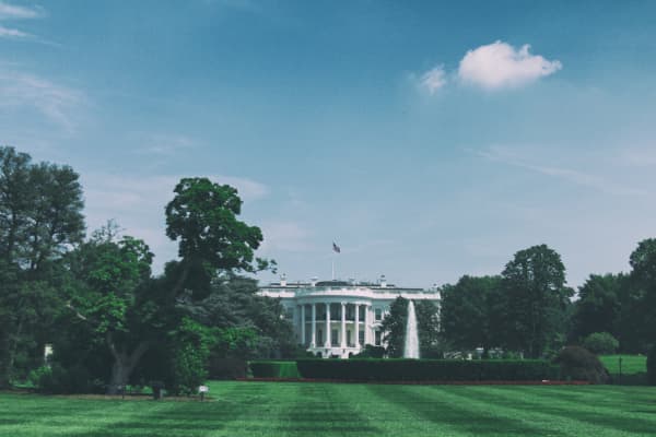 Photo of green grass in foreground with trees and the White House in the background